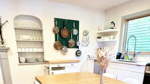 Une cuisine moderne avec une table à manger en bois, des chaises blanches et divers ustensiles de cuisine exposés sur le mur.