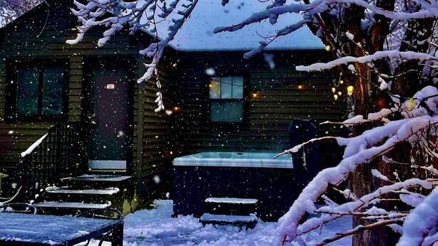 Une cabane en bois dotée d’un bain à remous, entourée d’arbres couverts de neige.