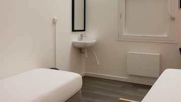 A small, modern room with two single beds, a white sink, and a window with a view.