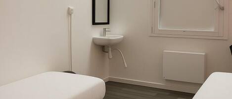 Una habitación pequeña y moderna con dos camas individuales, un lavabo blanco y ventana con vistas.