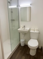 Un baño con ducha de vidrio, lavamanos blanco y retrete.