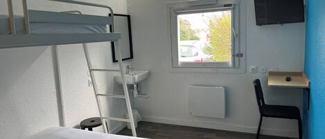 Une chambre avec des lits superposés, un bureau, une chaise, une fenêtre et un téléviseur fixé au mur.