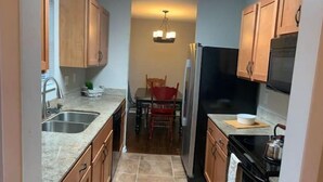 A narrow kitchen with wooden cabinets, a refrigerator, and a stove. - 3 blocks from AT&T Stadium 2 bedroom-sleeps 6 (Arlington)
