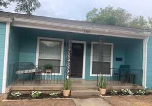 A teal house with the number 809, a front porch with steps, two potted plants, and a small garden area.