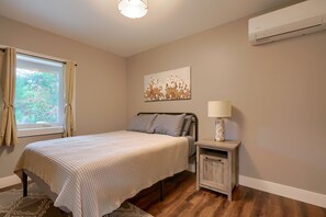 Une chambre à coucher comprenant un lit, une table de chevet, une lampe, un climatiseur et une fenêtre avec des rideaux.