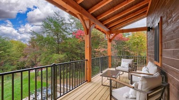 Terraza de madera con mobiliario exterior y barandilla, con vistas a un jardín con árboles y un cielo despejado.