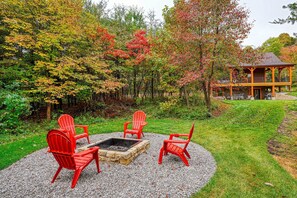 A circular seating area with red chairs and a stone fire pit surrounded by gravel, set in a lush garden with trees in autumn colors.