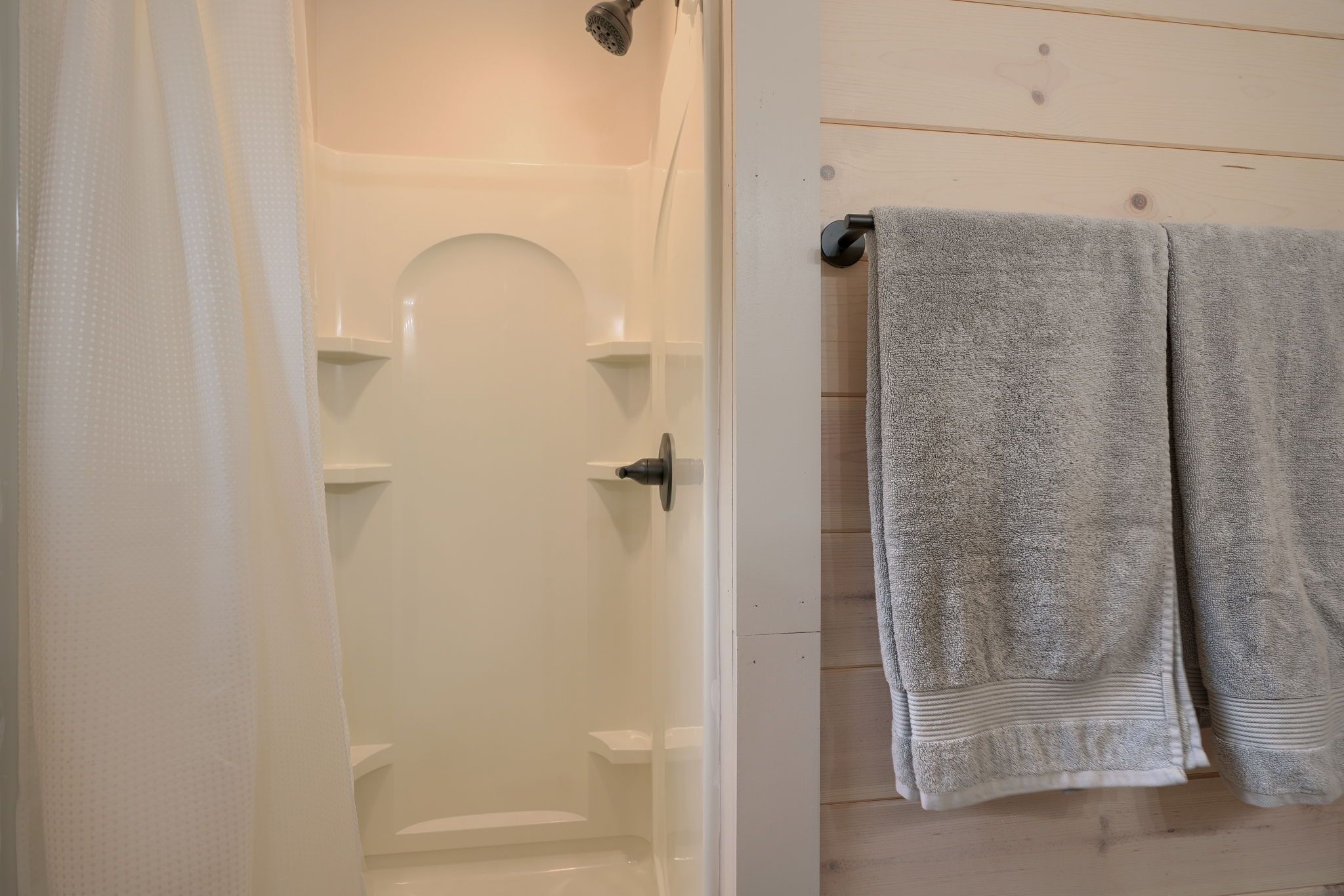 A bathroom with a shower, a towel rack with two towels, and a white door.