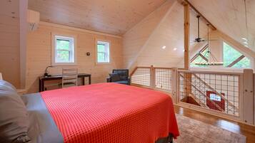 Un dormitorio con cama, escritorio y silla. Hay un balcón con barandilla y vistas al exterior.