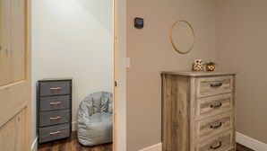 Una habitación con un armario de madera, un sillón informal gris y un pequeño aparador de madera con cajones.