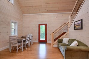 A wooden interior with a dining table and chairs, a green sofa, and a staircase.
