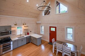 A spacious kitchen with modern appliances, a dining area with a red door, and large windows providing natural light.