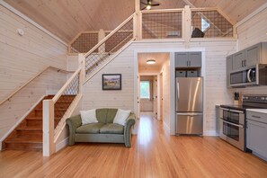 A spacious kitchen with stainless steel appliances, a wooden staircase, and a green sofa.