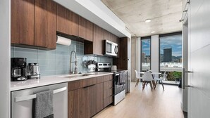 A modern kitchen with dark wood cabinets, a stainless steel refrigerator, and a large window offering a city view. - Gorgeous Downtown 1BD/1BA - BEST views + Amenities (Salt Lake City)