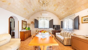 A spacious living area with a large wooden dining table, a sofa, a TV, and a chandelier. - 3584 Trullo Kalia by Barbarhouse (San Michele Salentino)