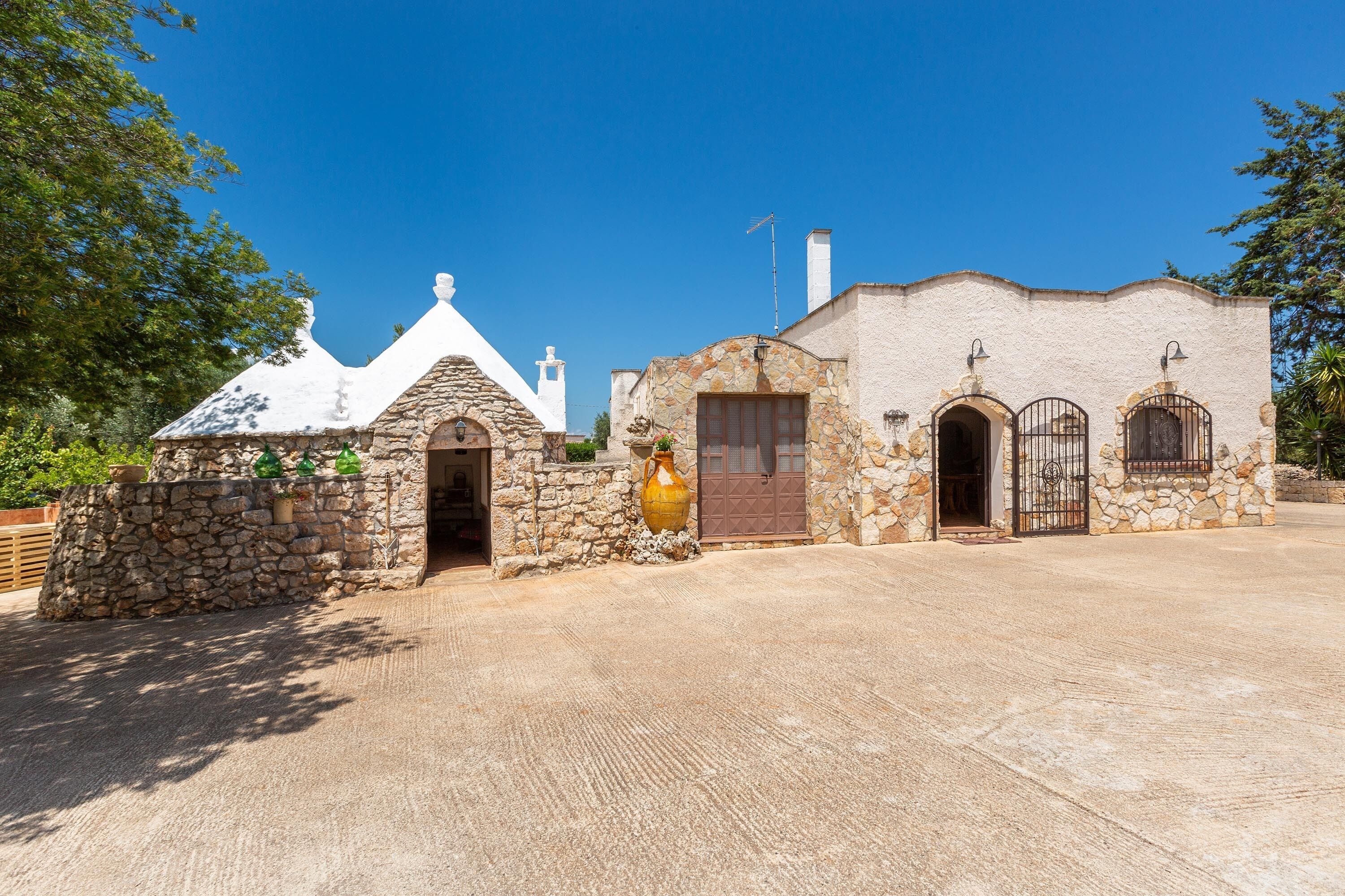 A traditional stone building with a tiled roof, a large ceramic pot, and a gated entrance.