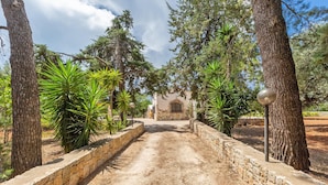A dirt pathway flanked by stone walls and trees, leading to a building with a stone facade and a window. - 3584 Trullo Kalia by Barbarhouse (San Michele Salentino)