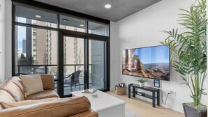 A modern living room with a leather sofa, a white coffee table, and a large flat-screen TV mounted on the wall. - Best Amenities Pool/Htub/Gym/Pking Downtown Views! (Salt Lake City)