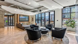A modern lounge area with a large screen, comfortable seating, and large windows offering views of the city. - Best Amenities Pool/Htub/Gym/Pking Downtown Views! (Salt Lake City)