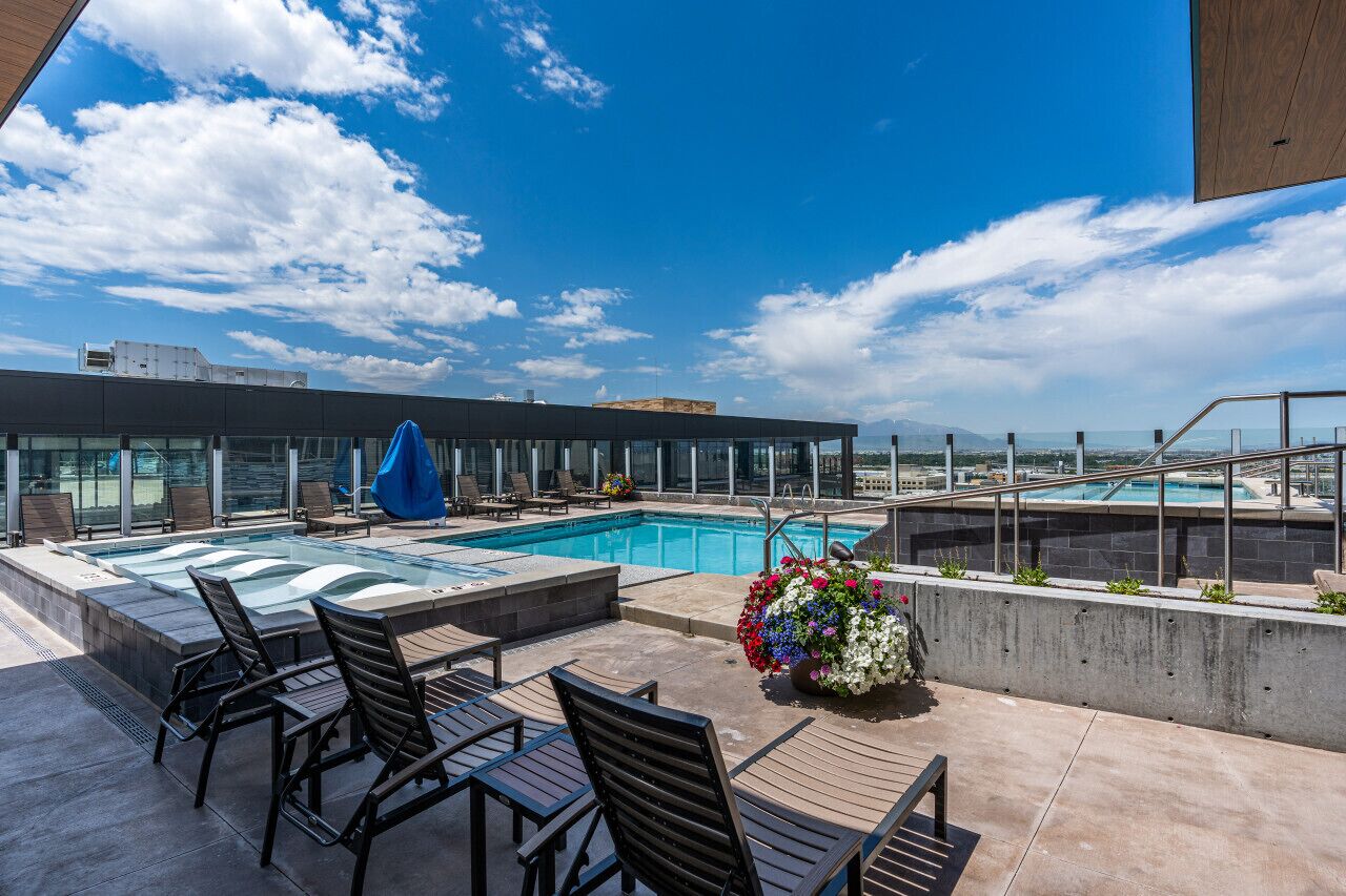 A rooftop pool area with a glass balustrade, lounge chairs, and a flower arrangement.