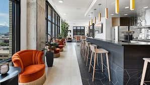 Eine moderne Hotelhalle mit einer langen Bar, Sitzgelegenheiten und großen Fenstern mit Blick auf die Stadt.