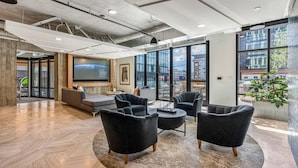 Ein moderner Lounge-Bereich mit großem Bildschirm, bequemen Sitzgelegenheiten und großen Fenstern mit Stadtblick.