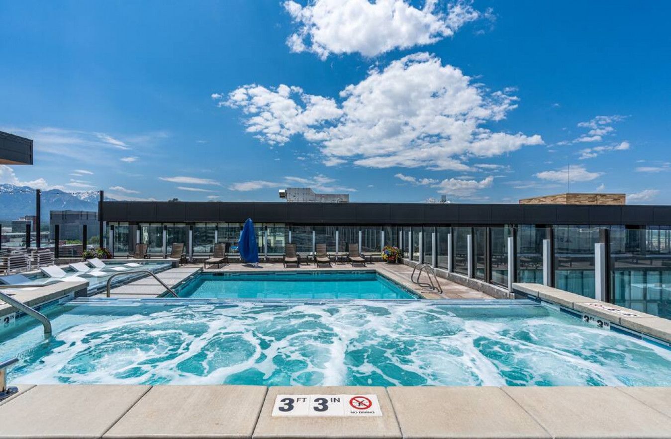 A rooftop pool with clear blue water, lounge chairs, and a glass-enclosed area with a mountain view.