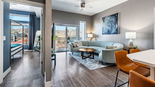 A modern living room with a sofa, coffee table, and chairs, a balcony with a view, and a ceiling fan. - Penthouse Apt - PoolGymHotTubPkg - View! (Salt Lake City)