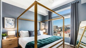 A four-poster bed with a city view, a bedside table with a lamp, and a nightstand with a plant. - Penthouse Apt - PoolGymHotTubPkg - View! (Salt Lake City)