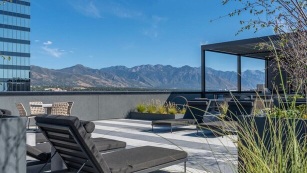 Eine Dachterrasse mit Sitzgelegenheiten im Freien, Blick auf Berge und ein modernes Gebäude im Hintergrund.