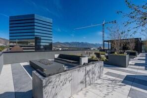 Terraço no telhado com áreas de estar, lareira e vista para montanhas e um edifício moderno.