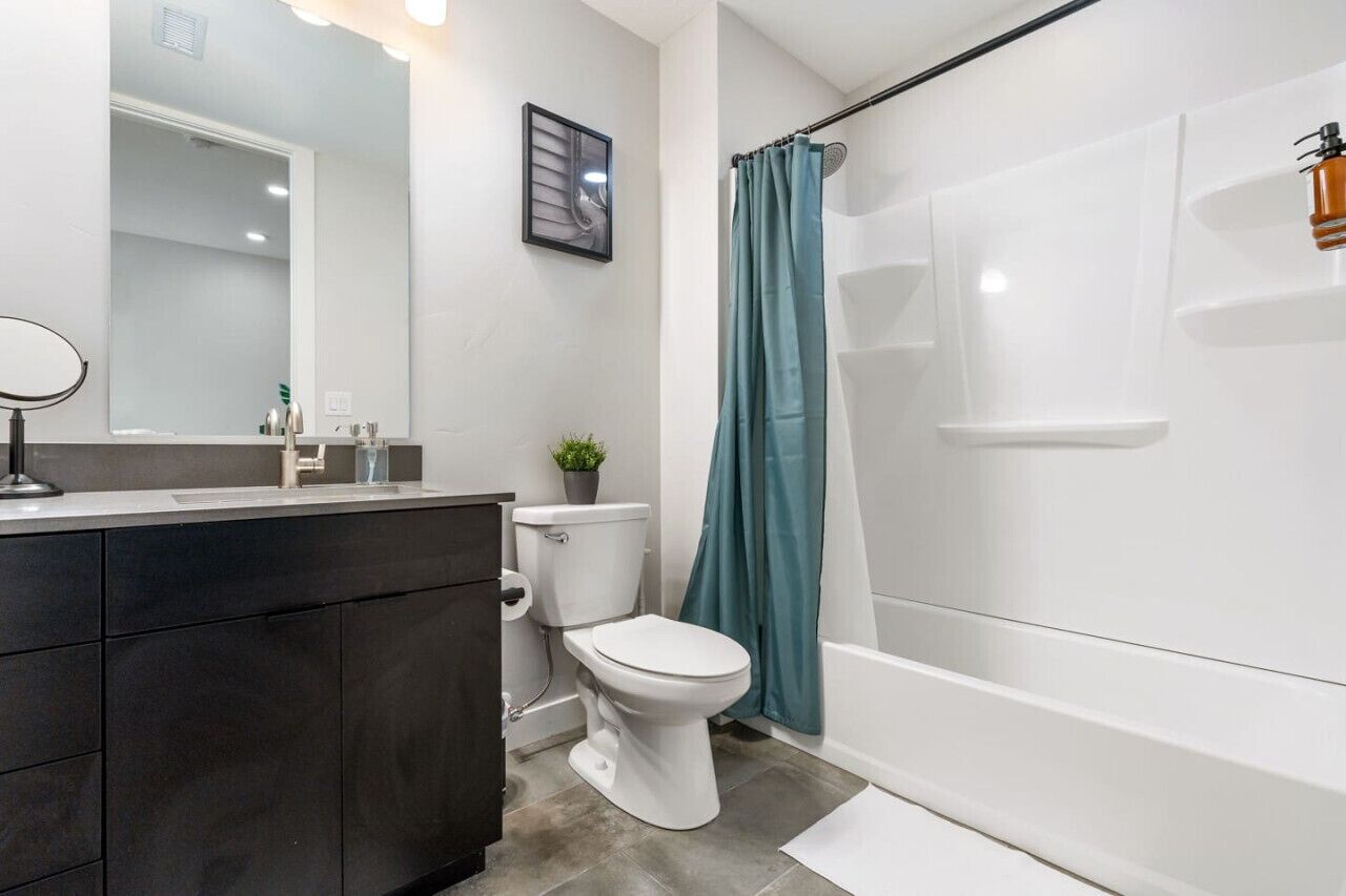 Une salle de bain moderne avec des toilettes blanches, un meuble-lavabo aux tons foncés, un grand miroir et une douche avec un rideau de couleur turquoise.