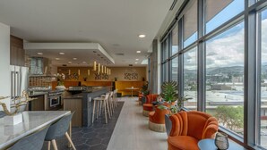 Un moderno vestíbulo de hotel con comedor, cocina y grandes ventanales que ofrecen vistas de la ciudad.