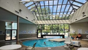 An indoor swimming pool with a glass ceiling, surrounded by lounge chairs and tables. - Sea Turtle (Myrtle Beach)