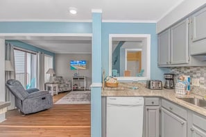 A modern kitchen with grey cabinets, a dishwasher, and a countertop with a toaster and coffee maker. - Sea Turtle (Myrtle Beach)