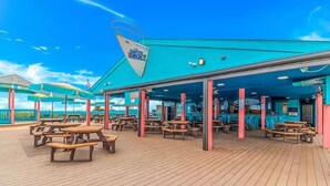 A covered outdoor deck with picnic tables and umbrellas, a turquoise building with a sign, and a clear blue sky. - Sea Turtle (Myrtle Beach)