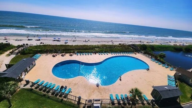 A beachside pool with lounge chairs, a sandy beach, and the ocean in the background. - Sea Turtle (Myrtle Beach)