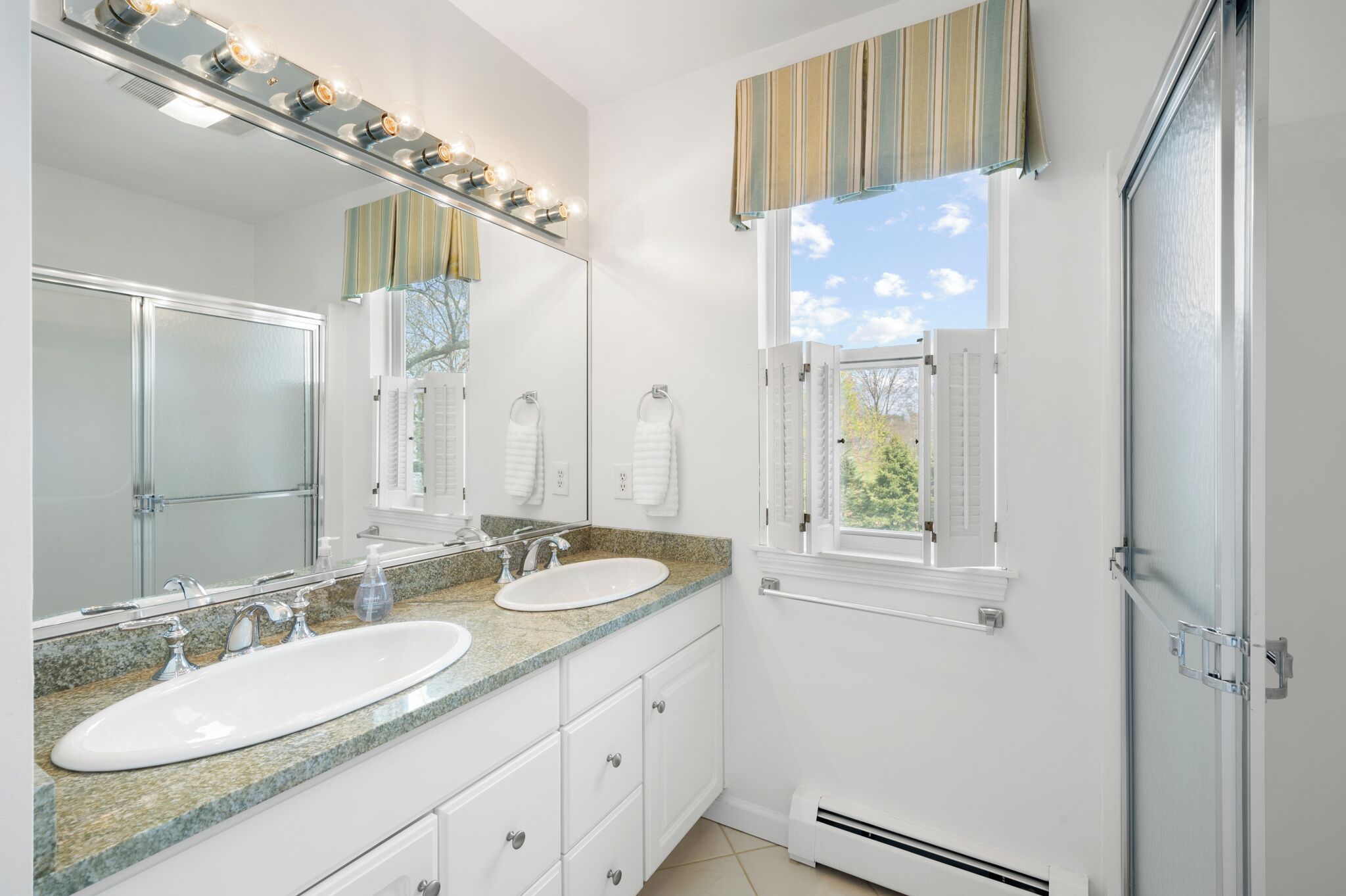 Un baño con dos lavamanos, un espejo grande y una ventana con contraventanas.