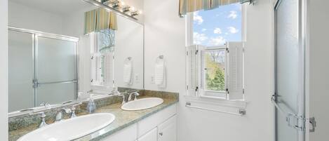 Un baño con dos lavamanos, un espejo grande y una ventana con contraventanas.