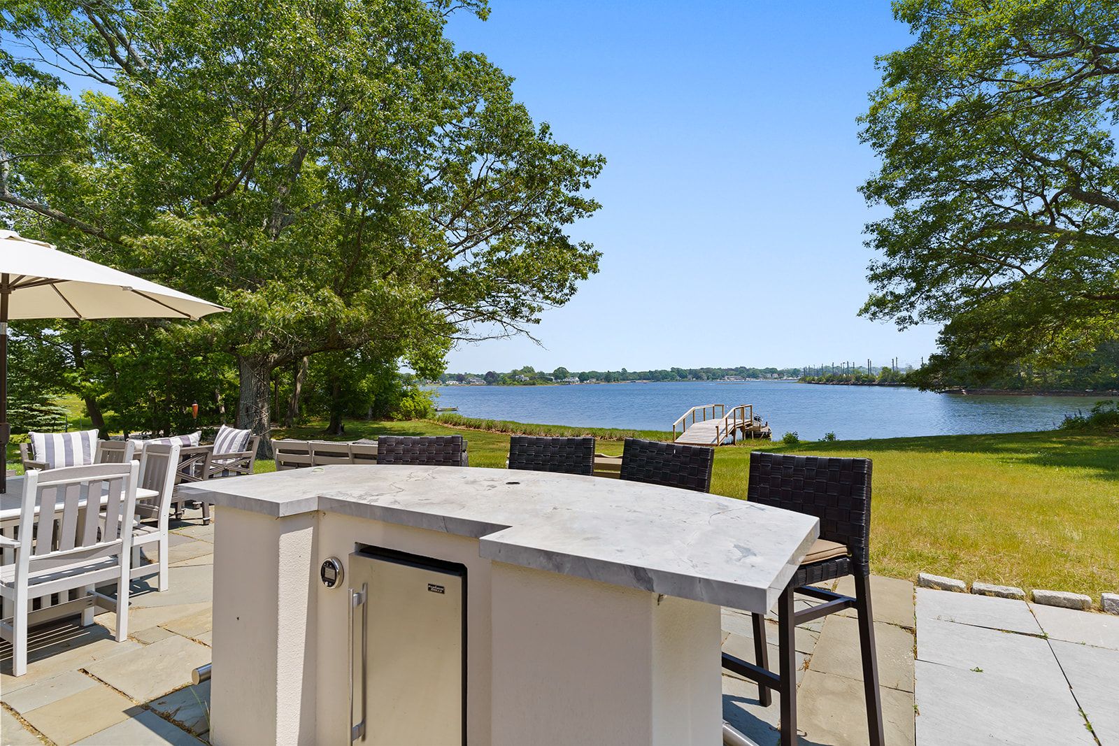 An outdoor dining area with a built-in bar, seating, and a view of a lake.
