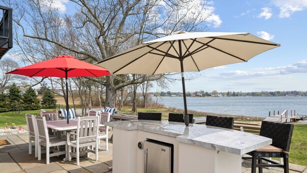 Un espace bar extérieur doté d’un réfrigérateur intégré, de deux parasols et offrant une vue sur un lac.