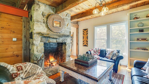A cozy living room with a stone fireplace, leather furniture, and a bookshelf. - Luxe 14-Acre Vermont Countryside Lodge! (Washington)