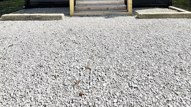 A modern building with a covered porch, a black door, and a gravel driveway.