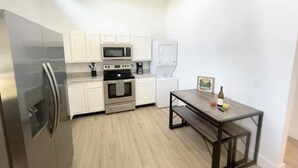 A compact kitchen with white cabinets, stainless steel appliances, and a wooden dining table.