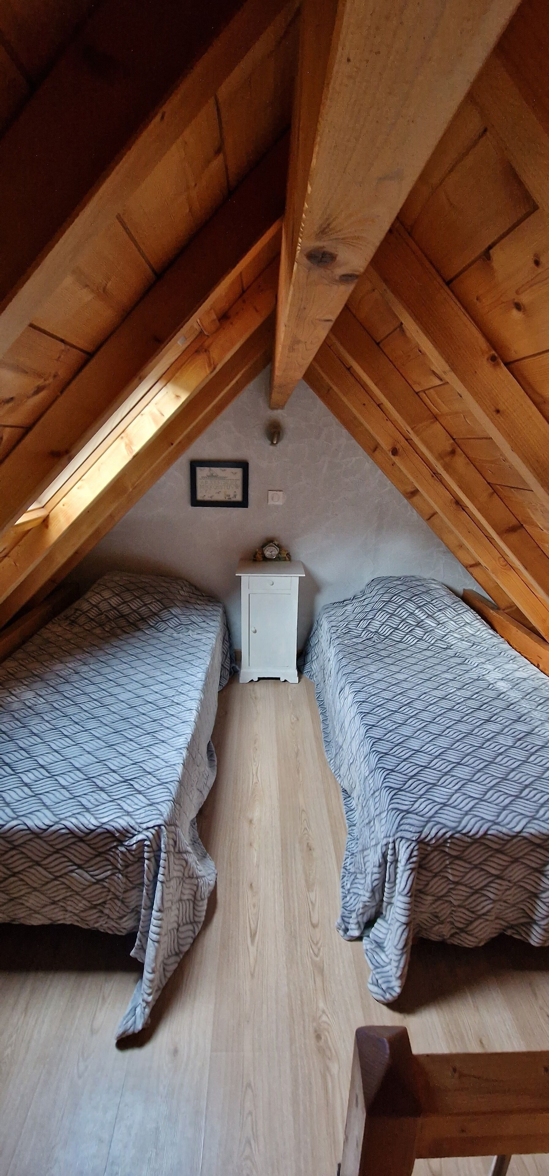Un pequeño dormitorio en el ático con dos camas, una mesita de noche y techo de madera.