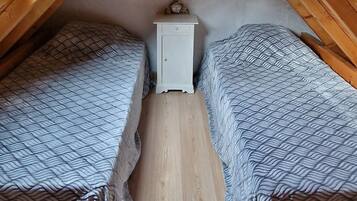 Un pequeño dormitorio en el ático con dos camas, una mesita de noche y techo de madera.