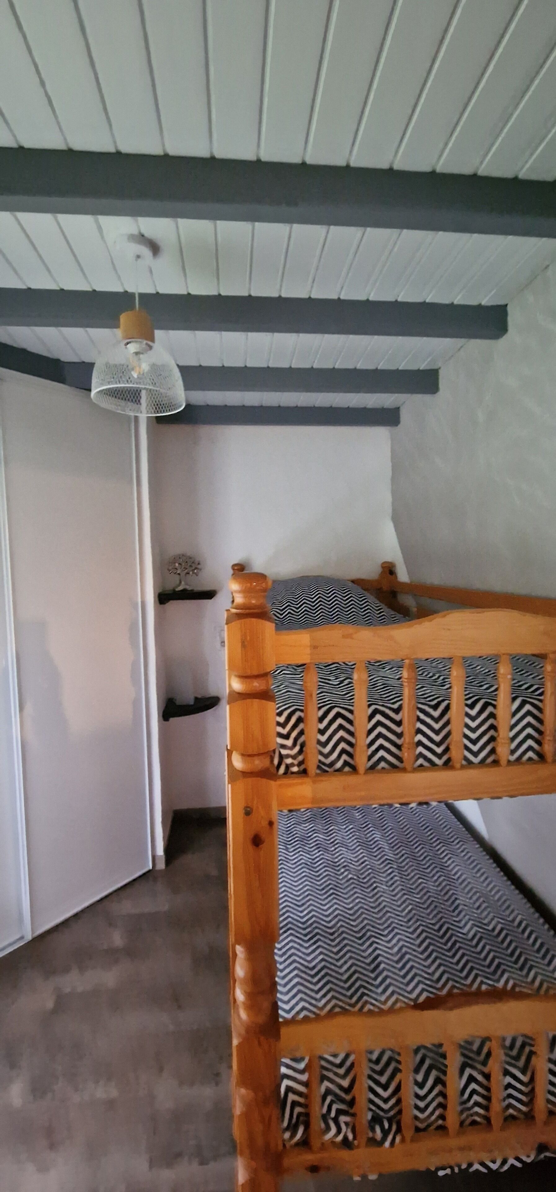A small room with a bunk bed, a single bed, a white wardrobe, and a hanging lamp.