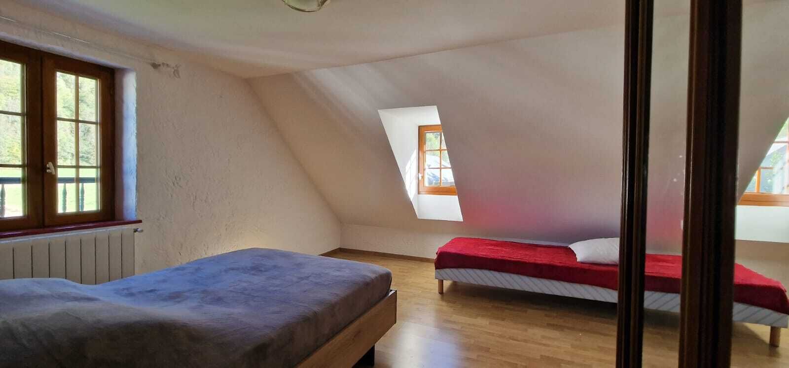 Ein kleiner Raum mit schrägem Dach, zwei Betten, einem Fenster und einer Heizung.