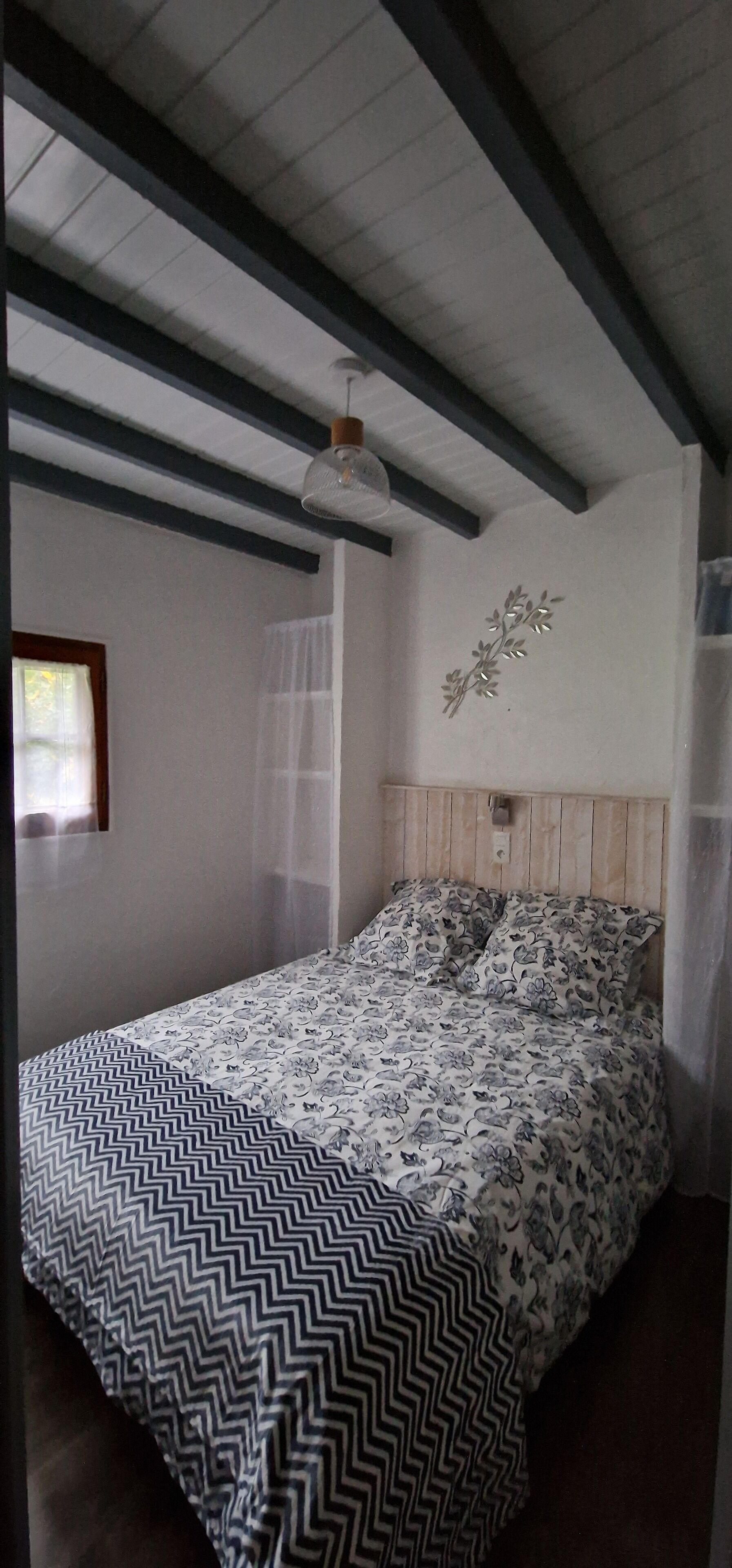 A bedroom with a bed, a ceiling fan, and a window with sheer curtains.