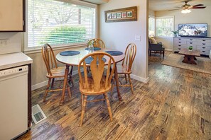 A dining area with a round table, four wooden chairs, a ceiling fan, and a kitchen with a dishwasher.